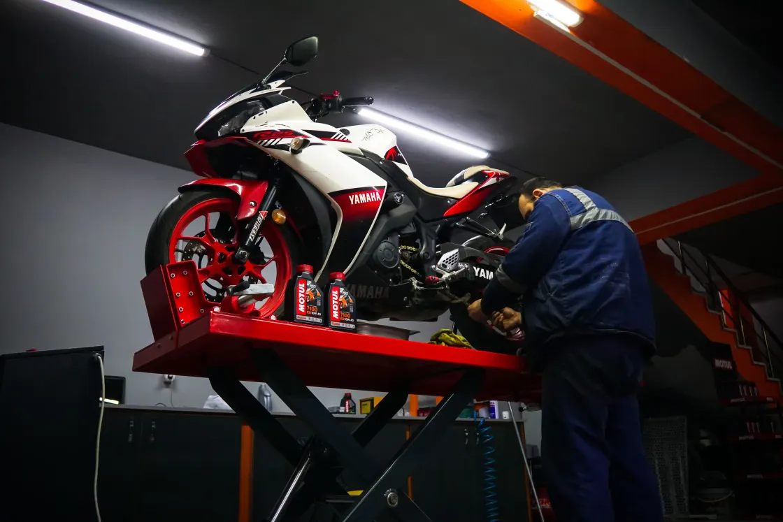 Mecânico trabalhando em uma moto esportiva sobre a plataforma elevatória da oficina