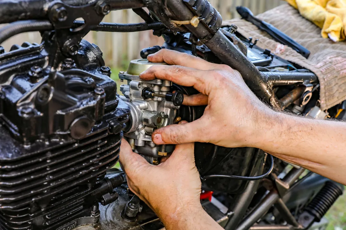 Mãos de mecânico ajustando o carburador de um motor de moto